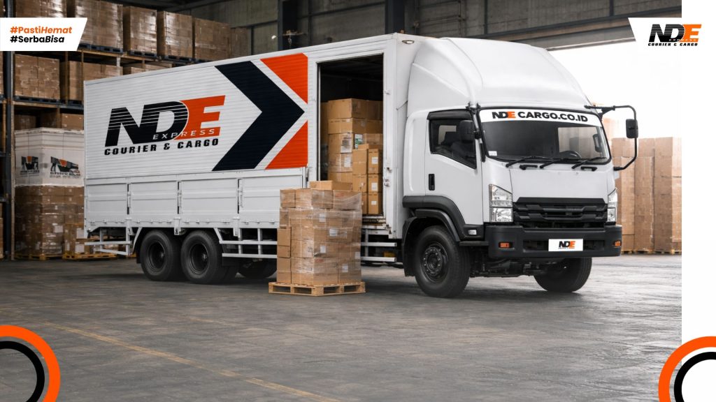 Truk NDE Cargo berada di dalam gudang dengan posisi menghadap ke luar, siap melakukan pengiriman barang logistik